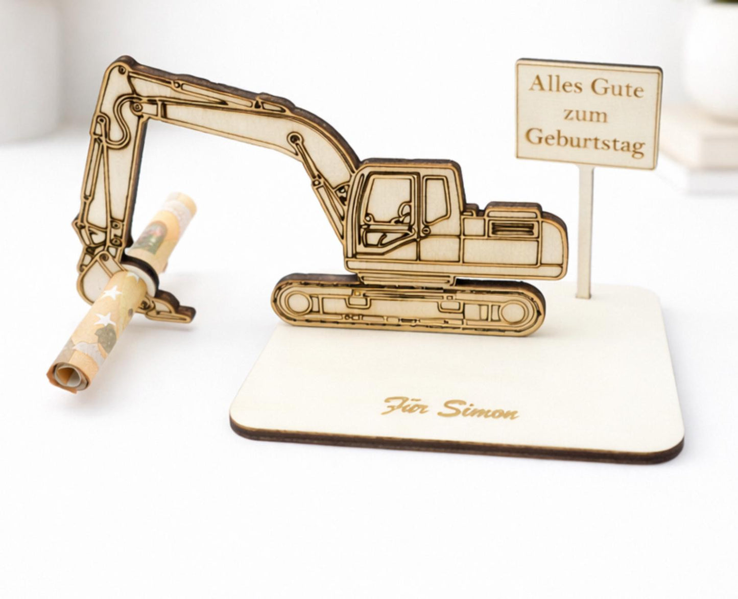 Nahaufnahme von dem personalisierten Geldgeschenk mit einem Bagger, einem Ortsschild und einer persönlichen Gravur auf der Grundplatte